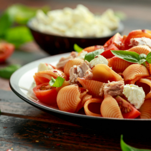 Conchiglie Tuna pasta with tomato sauce, feta cheese and basil on wooden table. healthy food