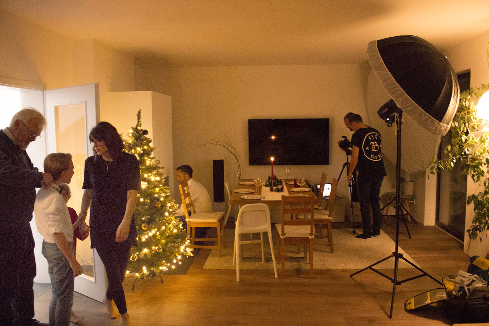 Die Crew beim Vorbereiten des Shootings. Opa richtet des Kragen des Enkels, Papa zündet den Kamin an und der Fotograf richtet das Licht ein.